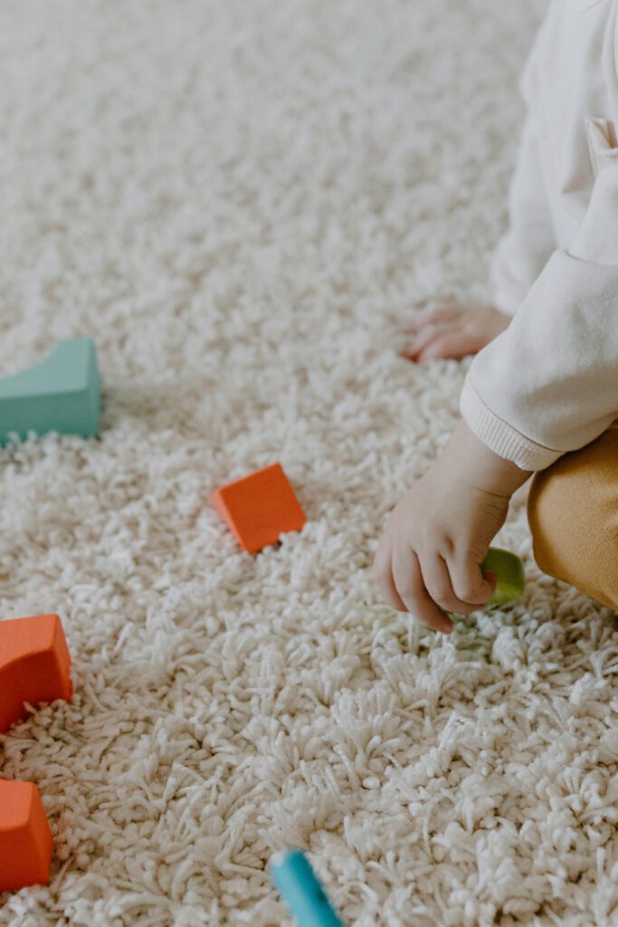 A child's hand arranging wooden blocks on a carpet, focusing on playful learning.